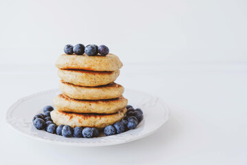 Stack of homemade small thick pancakes served with fresh blueberries.