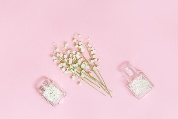 Small flowers of lilies of the valley and glass bottle with dry petals on soft pink background with copy space for text. Spring time and aromatherapy. Spa flat lay.