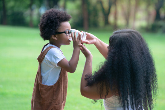 Mother Feeds The Dark Skinned Boy  From The Glass Of Milk At Park