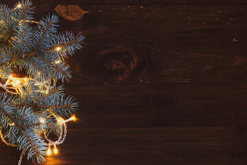 Christmas background of glowing ice yellow garland and branches of a beautiful Christmas tree on a brown dark wooden background. Natural background for the Christmas holiday. copy space.