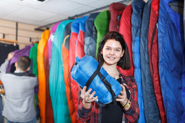 Fototapeta premium Female customer examining sleeping bags in sports equipment store