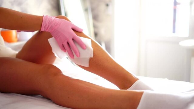 A female cosmetologist treats the leg of a young girl before the hair removal procedure. Shugaring. Master shugaring sprinkles disinfectant solution on the leg before depilation.