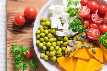 Salad with pumpkin, parsley, tomatoes and feta cheese, healthy food for diet. Top view, close-up