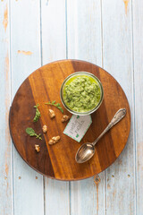 Arugula Chive Basil Pesto served in a glass jar with nuts . Photographed from front view on a black/light blue background.