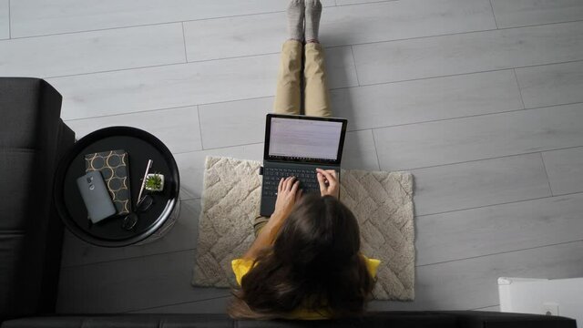 Top view of female freelancer sitting on floor near sofa at home and working on laptop computer. Woman typing on laptop. quarantine concept work online