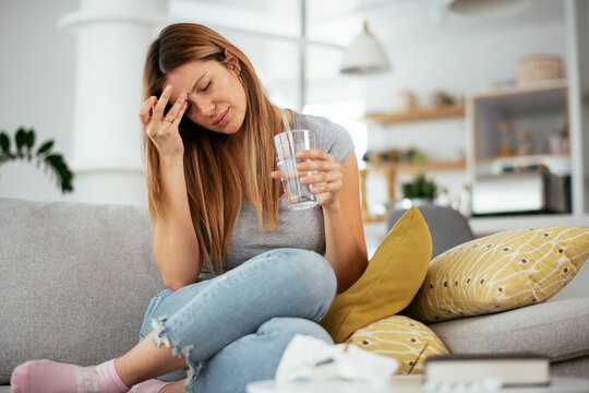 Young woman sick in bed holding glass of water..