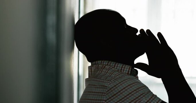 Troubled black man leaning on wall in anguish, silhouette of African person in desperation