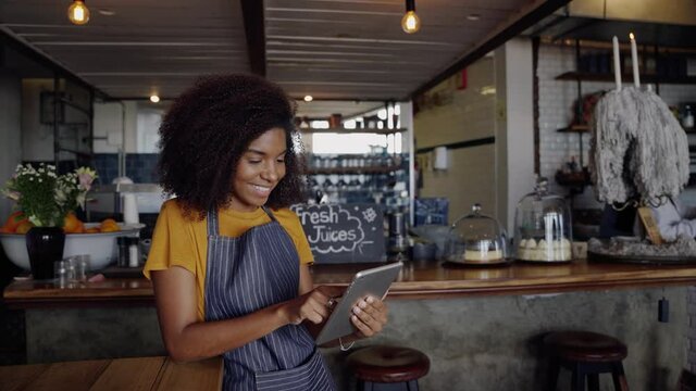 Beautiful waitress using face ID to unlock tablet standing in funky cafe 