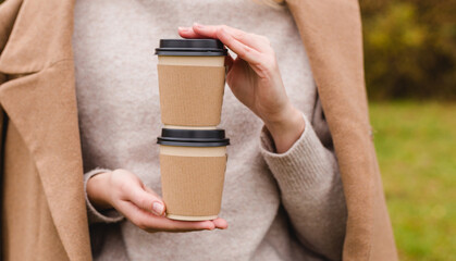 Woman holds two paper coffee cups. Take away or delivery concept. Copy space. Autumn lifestyle. Place for your text or logo on mug, mockup