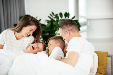 Obraz premium Young family enjoying in bed. Happy parents with sons relaxing in bed.