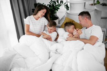 Obraz premium Young family enjoying in bed. Happy parents with sons relaxing in bed.
