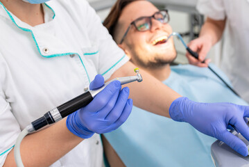 Female dentist with preparing to polishes teeth to a male patient in the dental clinic.