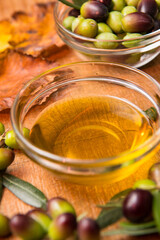 Extra virgin olive oil in a clear bowl on a wooden background and a bowl of olives and olive branches