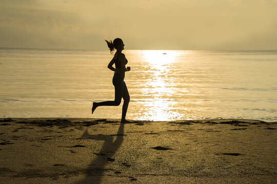 Silhouette of Asian girls  jogging on the beach at sunrise in morning .Summer Holiday and sport concept.