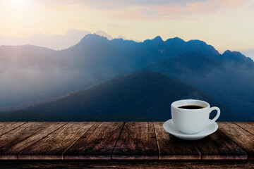 White cup of hot coffee on wooden table with mountain fog background