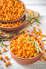 Sea buckthorn berries in small organic wooden bowl, with sea buckthorn branches on white wooden desk background