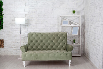 Living room interior with gray sofa against white brick wall. Modern lamp, shelving with empty photo frames and green plants in pots. Copy space