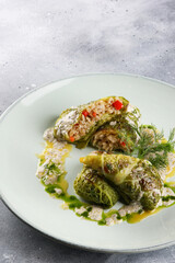 Russian and Ukrainian cuisine. Lean cabbage rolls with rice, red pepper, dill and sauce on a light plate on a gray background. Restaurant menu. Background image, copy space