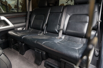 Rear seats of the car for three passengers in the back of an SUV covered in black leather with the armrest folded down before dry cleaning and washing in a auto workshop.