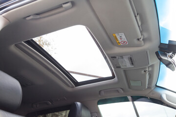 View of the ceiling of the car with a transparent glass hatch for airing, opening in summer while driving fast in the gray cabin of the vehicle. Sunroof on light coloured beige roof.