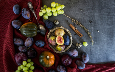 Fresh fruits and vegetables on a table. Top view photo of grapes, pumpkins, plums and figs. Grey textured background. Autumn still life.