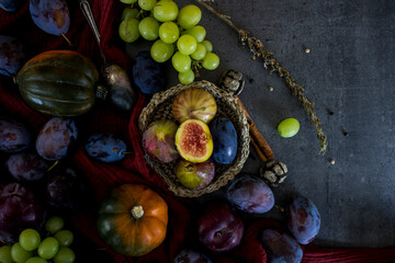 Fresh fruits and vegetables on a table. Top view photo of grapes, pumpkins, plums and figs. Grey textured background. Autumn still life.