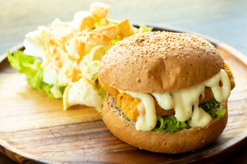 Fried fish fillet burger with vegetable salad on wood plate background