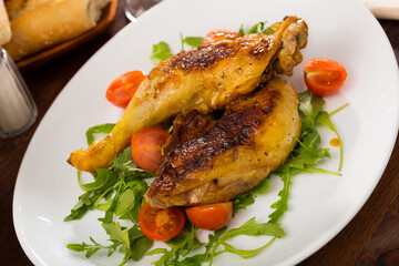 Roasted chicken legs with golden crust served with cherry tomatoes and arugula on plate