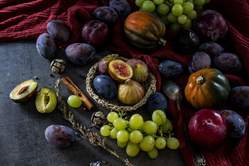 Fresh fruits and vegetables on a table. Top view photo of grapes, pumpkins, plums and figs. Grey textured background. Autumn still life.