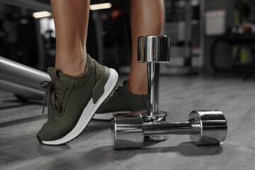Fototapeta na wymiar Sport concept. Close up image of a female legs in sneakers with dumbbell next to it