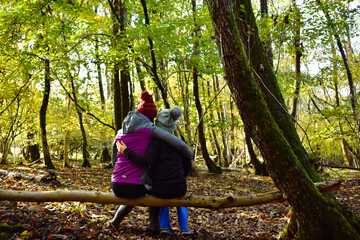 Fototapeta premium Autumn scene of two children sitting on a log in the woods