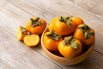Persimmon fruit in bowl on wood table.