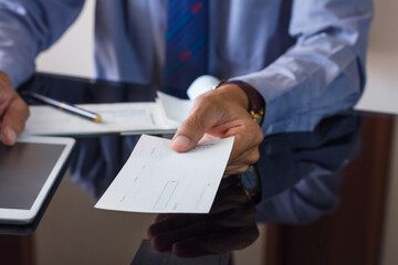 Business man or manager in suit hand  giving bank check to colleague with checkbook on the desk at office. Payday and payment by cheque concept