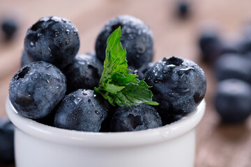 Ripe blueberries in drops of water with a leaf of fragrant mint on a wooden background.