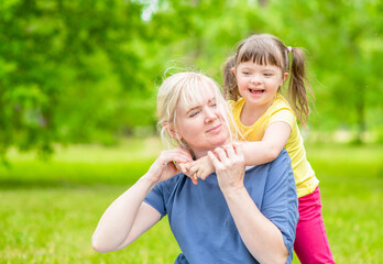 Mother and joyful little girl with special needs have a fun in summer park. Empty space for text