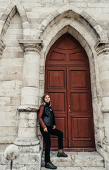 Fototapeta na wymiar young woman in a leather jacket near the entrance to the ancient wooden door of a gothic temple
