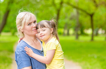 Portrait of a mother and little girl with special needs in summer park. Empty space for text