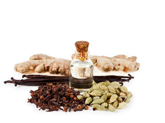 Bottle of oil with bourbon vanilla beans, cloves, ginger roots and green cardamom isolated spices on a white background.