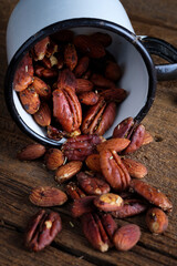 Enameled mug with spilled nuts on a wooden background. Salted pecans and almonds. Beer snack.