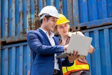 Engineer worker or technical women standing with her boss in the container yard shipping area. A man holding a laptop and discuss on work. Successful on project. Industrial and import-export concept