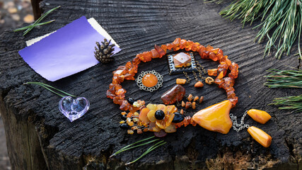 Amazing  vintage Baltic amber brooches surrounded by an orange amber necklace, empty greeting card  and a glittering lilac glass heart as decoration lie on a stump. Romantic festive composition.