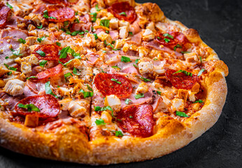 Pizza with Mozzarella cheese, salami, chicken meat, bacon, ham, Tomato sauce, pepper, spices. Italian pizza on Dark grey black slate background