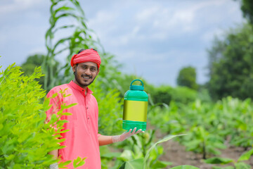 Young indian farmer showing fertilizer bottle at green field