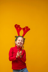 Happy little girl 4 years old in reindeer antlers on a bright yellow background.
