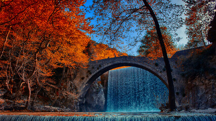 old arched bridge in front of a waterfall in autumn