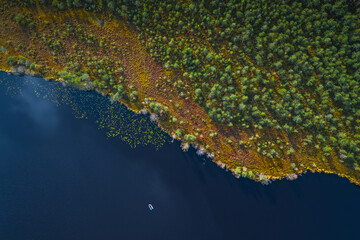 Aerial view of blue lake with a fishing boat and green forests