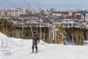 Happy smiling man in a ski suit climbs the mountain on skis on a snow-covered slope using a drag...