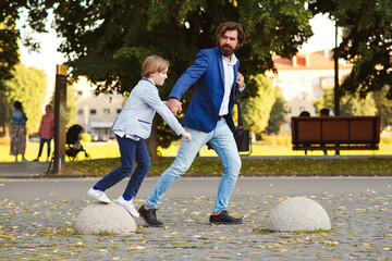 Happy father and son having fun together on a walk. Fashionable dad and kid running in summer park.