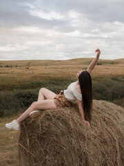Young woman in a wheat field. The brunette sits on a haystack.