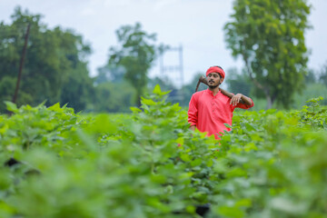 Young indian farmer holding farm equipment in hand at cotton field